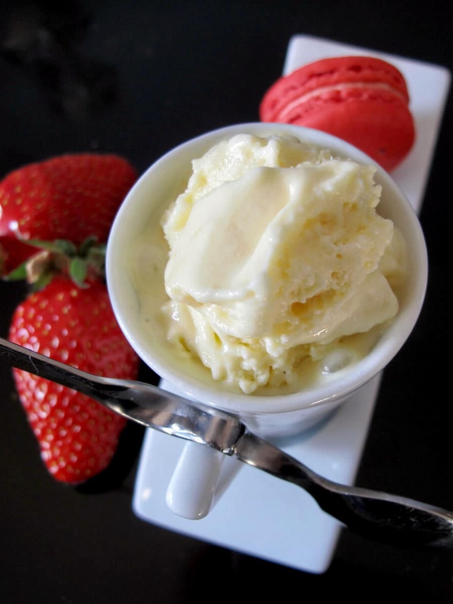 cup of creamy lemon ice cream served with strawberries and a strawberry macaron