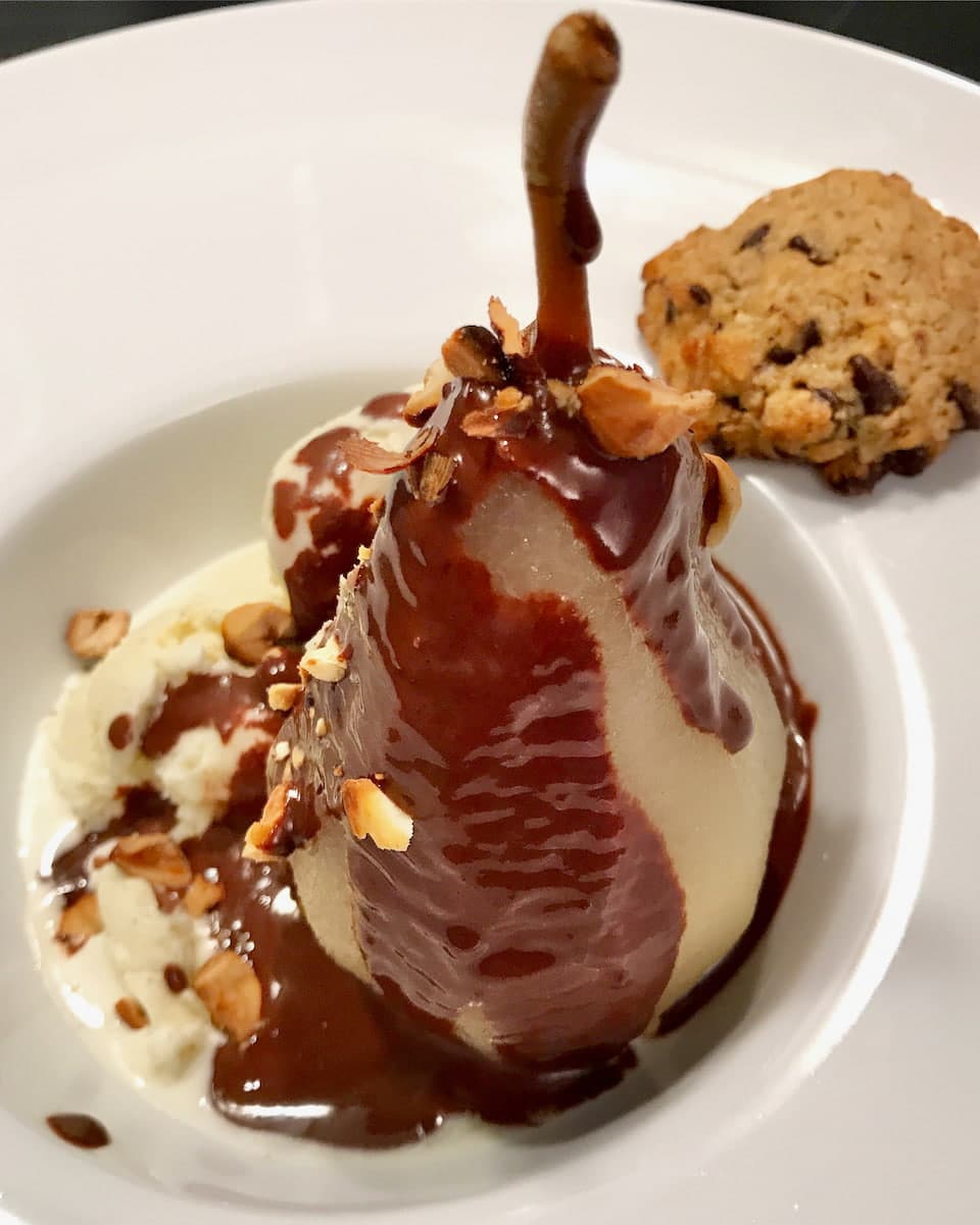 whole poached pear on vanilla ice cream, toasted nuts and covered in chocolate sauce