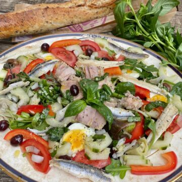 plate composed of a classic French salad Nicoise with many ingredients next to a basil plant and French baguette